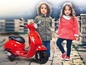 Dvě děti pózují vedle červeného dětského skútru Vespa.