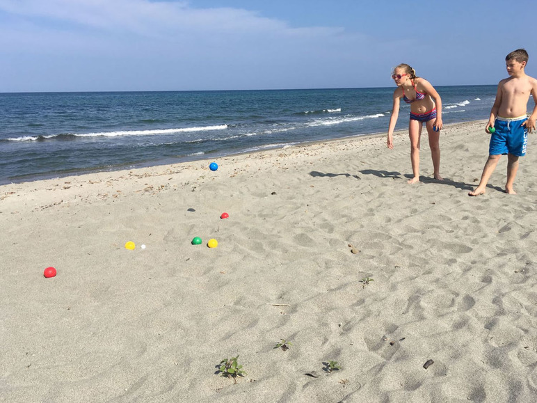 Dvě děti hrají pétanque na písčité pláži.