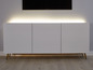 Bílá TV skříňka se zlatými nohami a LED osvětlením.
