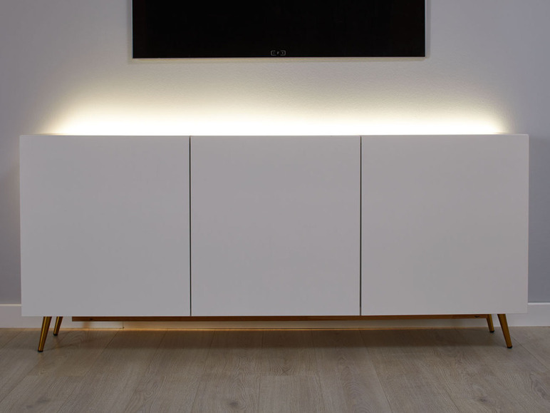 Bílá TV skříňka se zlatými nohami a LED osvětlením.