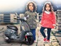 Dvě děti stojící vedle šedého skútru Vespa.