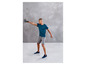 Muž v modrém tričku a šedých šortkách cvičí s kettlebell.