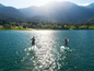 Dvě osoby paddleboarding na jezeře s výhledem na hory.