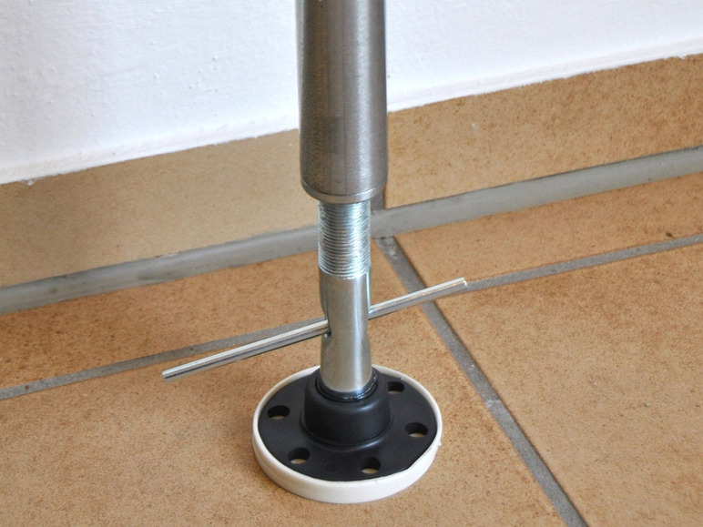 Kovový sloup se závitem a černou základnou na dlaždicové podlaze.