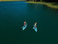 Dvě osoby pádlují na nafukovacích paddleboardech na jezeře.