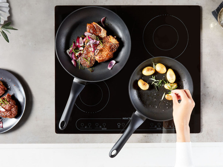 Steak s červenou cibulí a brambory v pánvích na indukční desce.