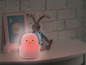 Růžová noční lampička ve tvaru tučňáka na bílém stolku.