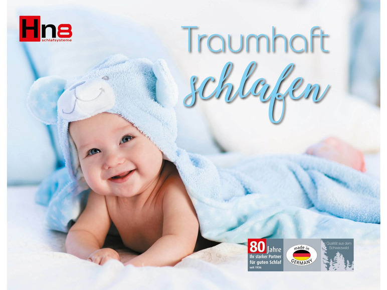 Dítě v modrém spacím pytli s textem 'Traumhaft Schlafen' a značkou 'Hna Schlafsysteme'.