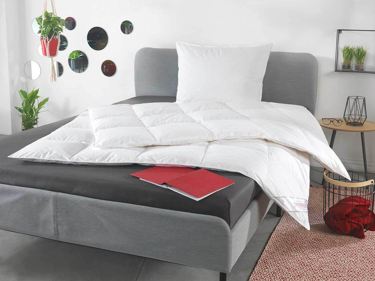 Bílá peřina a polštář na šedé posteli.