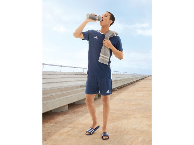 Muž v šortkách a tričku Adidas pije vodu na molu.