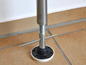 Kovový sloup se závitem a černou základnou na dlaždicové podlaze.