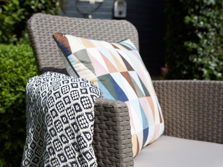 Wickerová židle s geometrickým polštářem a pruhovanou dekou.