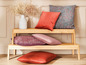 Dřevěná lavice s různými polštáři v červené, růžové a šedé barvě.