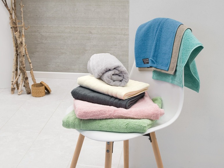 Hromádka ručníků a osušek, včetně modrého ručníku značky 'Kleine Wolke'.