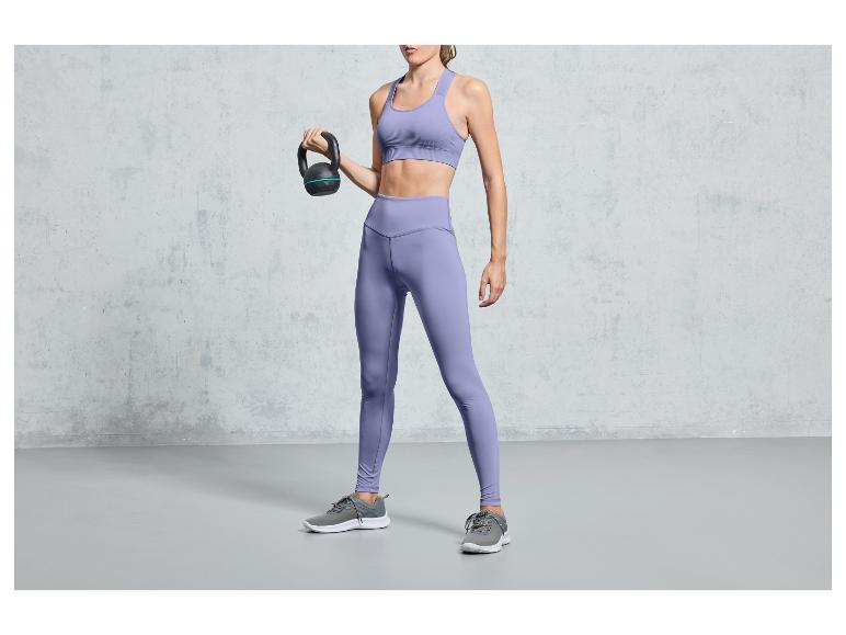 Žena ve fialovém sportovním oblečení drží kettlebell.