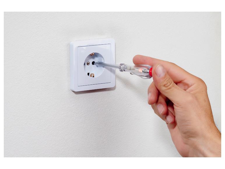 Ruka drží zkoušečku napětí v elektrické zásuvce.