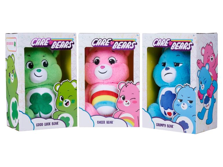 Tři plyšové hračky Care Bears v krabicích: Good Luck Bear, Cheer Bear a Grumpy Bear.
