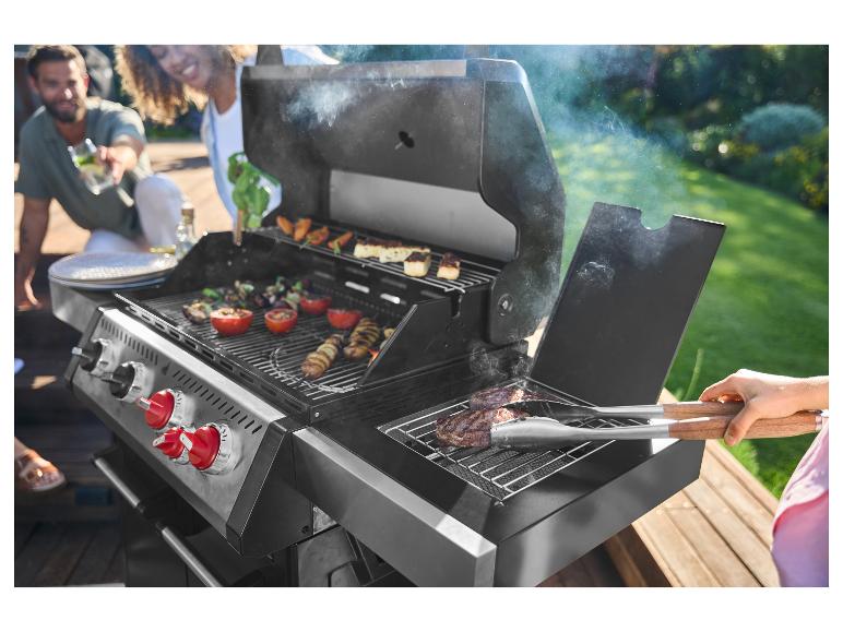 Přátelé grilují maso a zeleninu na plynovém grilu venku.