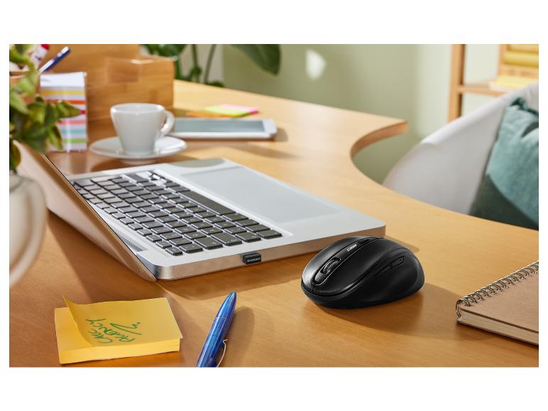 Bezdrátová myš, notebook a kancelářské potřeby na stole.
