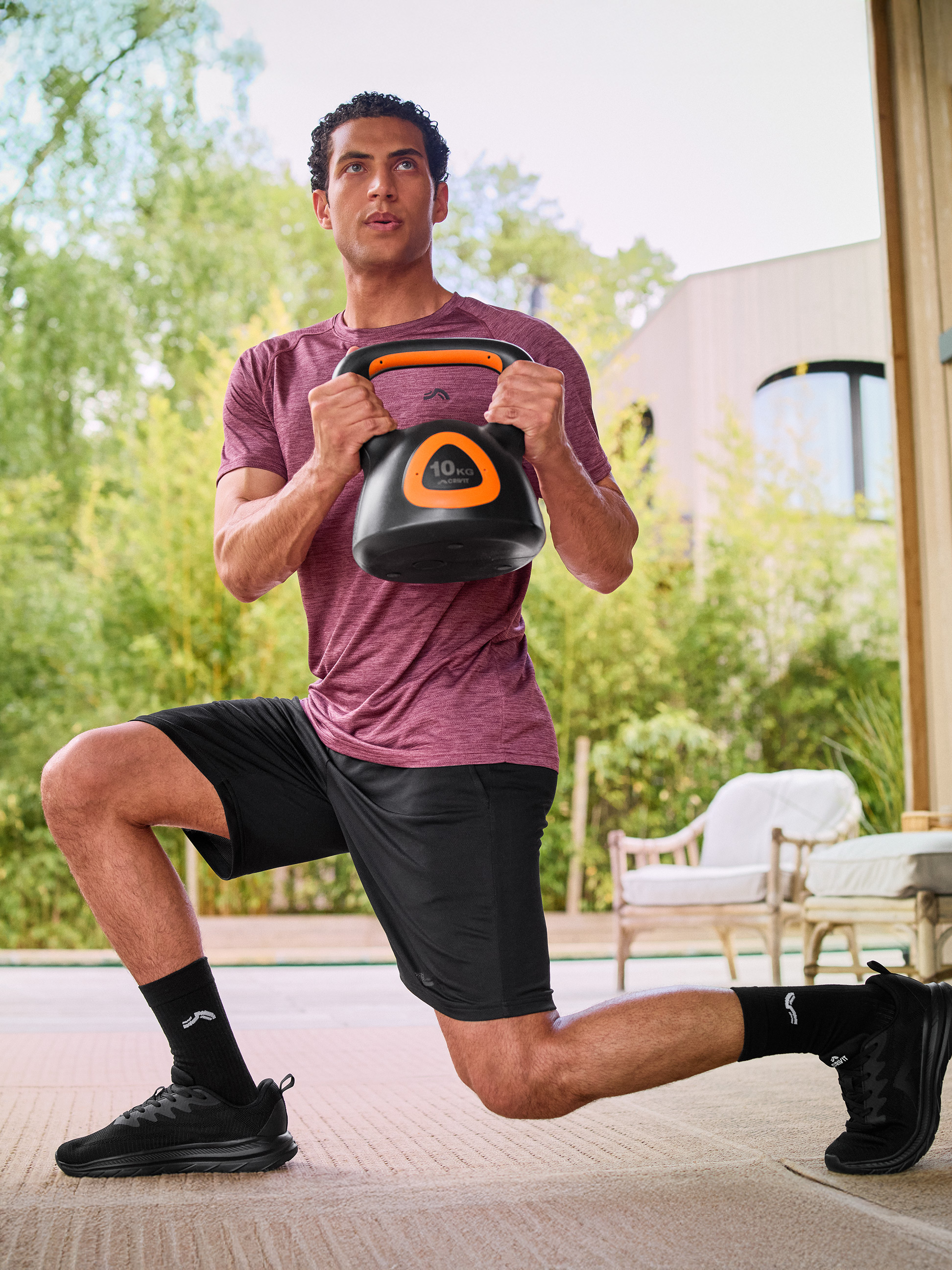 Muž ve sportovním oblečení dělá výpad s černým 10 kg kettlebellem.
