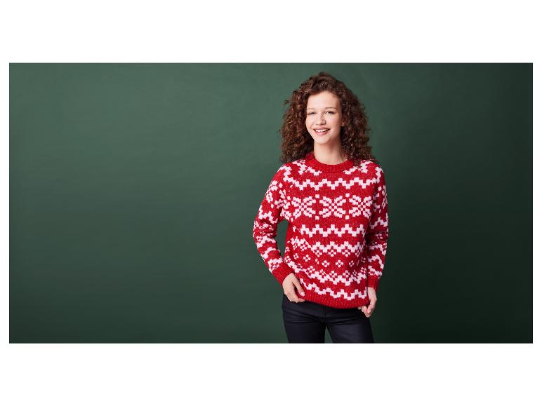 Žena v červeném svetru s vánočním vzorem před zeleným pozadím.