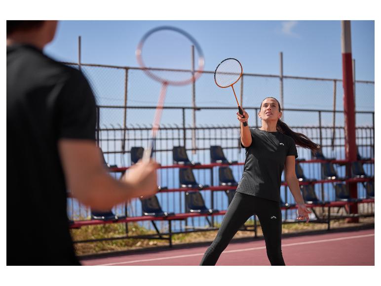 Žena a muž hrají badminton na venkovním kurtu, oblečeni v černém sportovním oblečení.