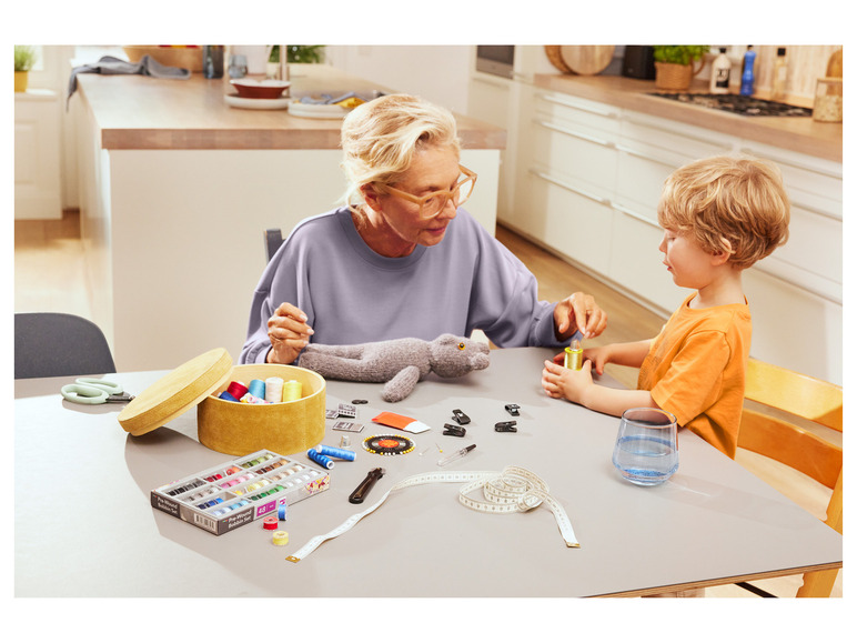 Dospělý a dítě si pomáhají s šitím pomocí šicích nití, měřicího pásma a šicí krabičky.