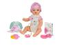 Panenka Baby Born s doplňky, jako je láhev, dudlík a kniha.
