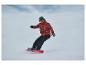 Snowboardista v červené vzorované bundě a černých kalhotách, na červeném snowboardu.