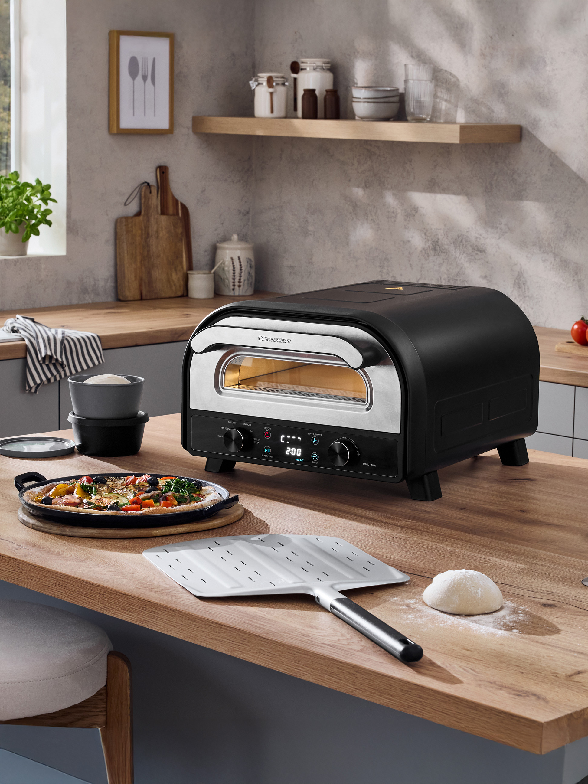 Černá pec na pizzu na dřevěné desce s čerstvě připravenou pizzou a těstem.