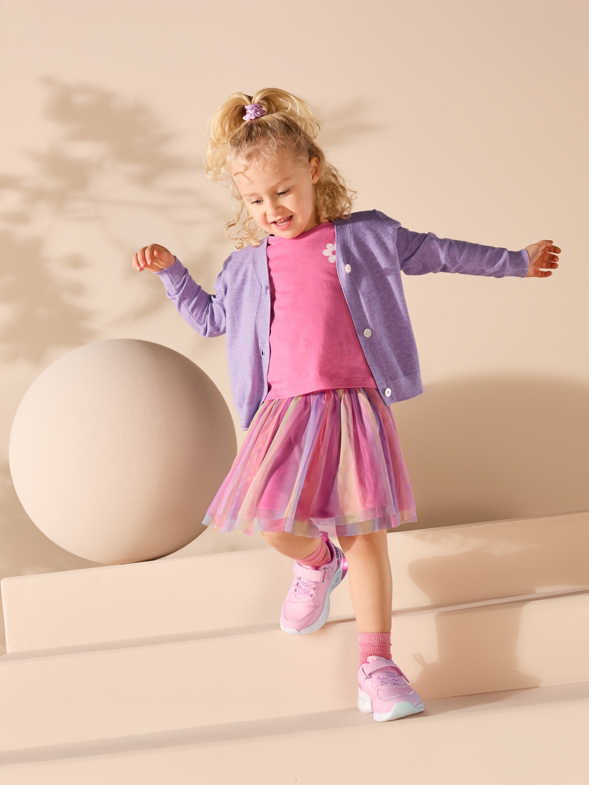 Holčička v růžovém tričku, fialovém kardiganu a barevné tylové sukni.