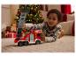Dítě si hraje s červeným hasičským autem na podlaze před vánočním stromkem.