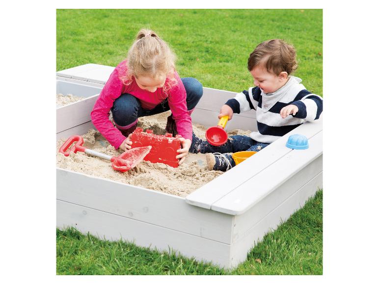 Dvě děti si hrají v dřevěné pískovišti.