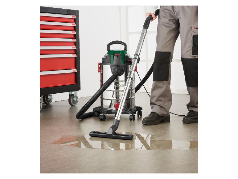 Muž čistí kaluž vody mokrým/suchým vysavačem vedle skříně na nářadí.