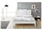 Bílá postel s peřinou a polštářem, čtecí lampa a odkládací stolek v moderní ložnici.