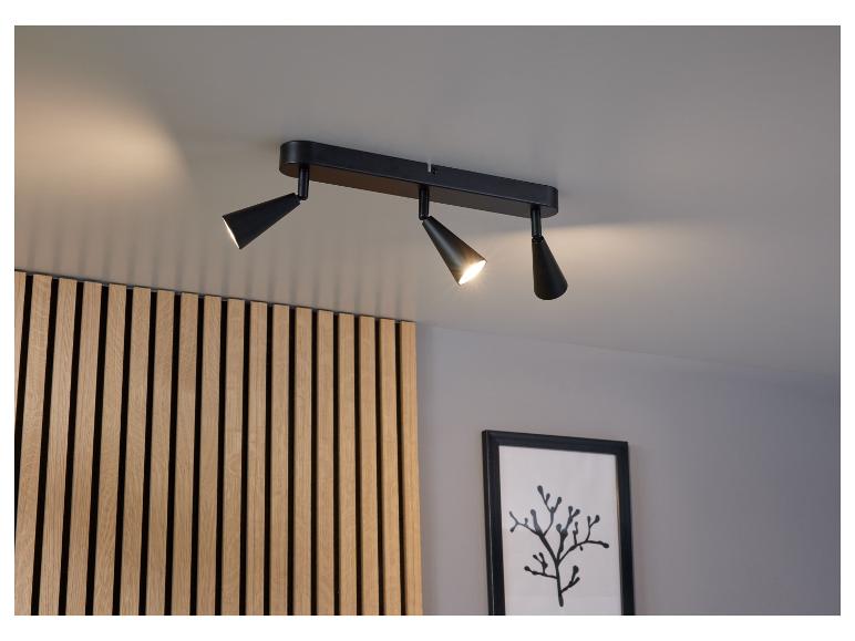 Černá stropní lampa se třemi reflektory namířenými na dřevěnou stěnu.