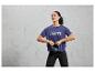 Žena v modrém sportovním tričku s nápisem 'Break the Limits' drží černou kettlebell.