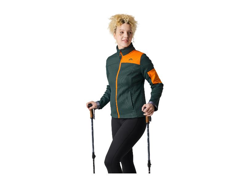 Žena ve sportovní bundě Craft a s trekovými holemi.