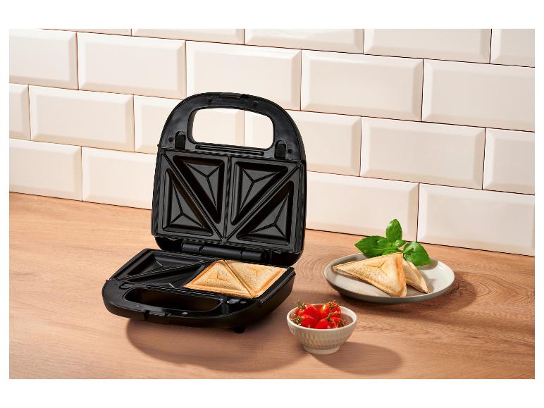 Otevřený sendvičovač s hotovými toasty, rajčaty a bazalkou.