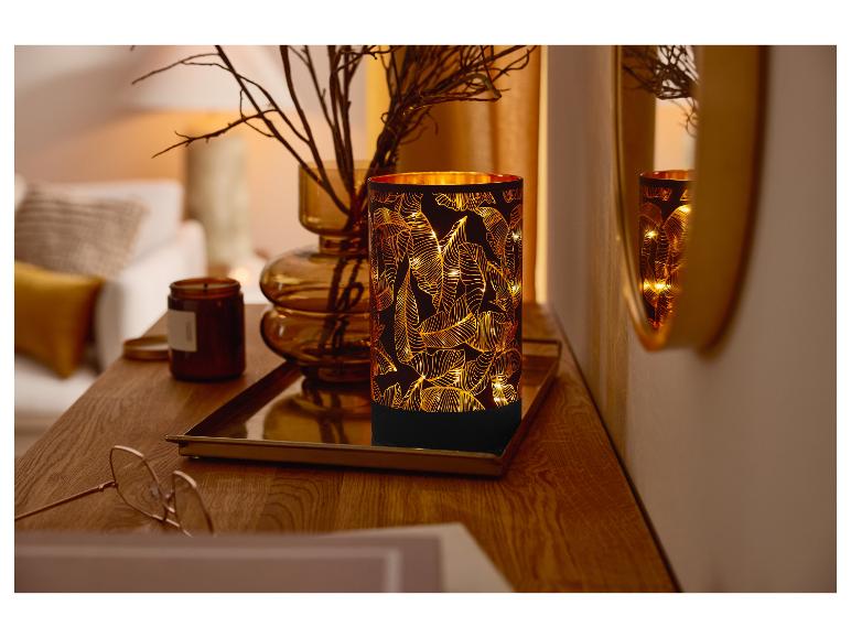 Osvětlená stolní lampa s motivem listů na dřevěném stolku.