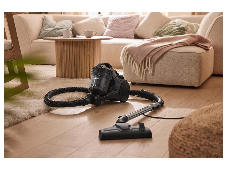 Vysavač SilverCrest na dřevěné podlaze, vedle chlupatého koberce a pohovky.