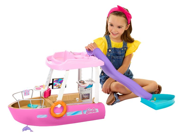 Usmívající se dívka si hraje s růžovou hračkou lodi Barbie, se skluzavkou a doplňky.