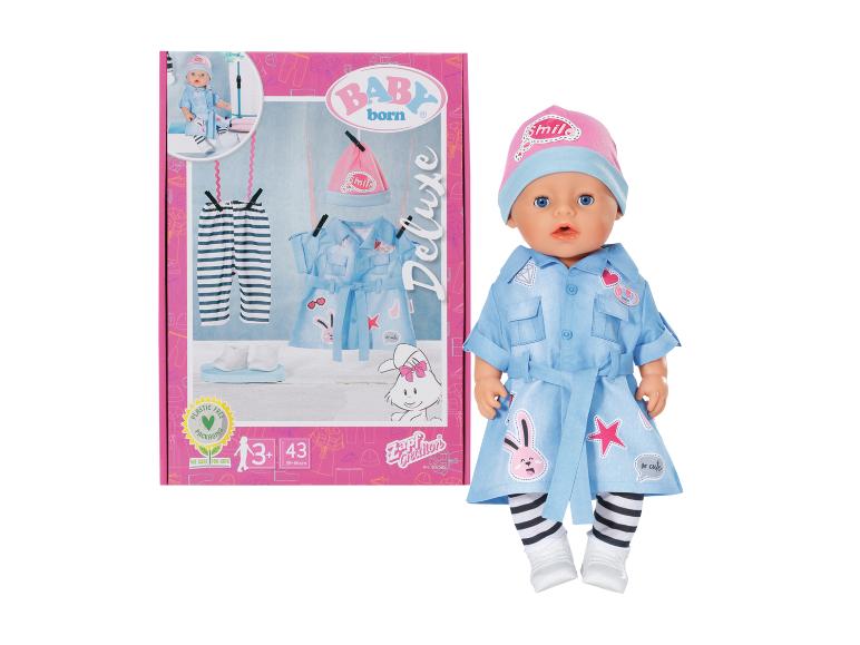 Panenka BABY born Deluxe v modrých šatech se zajíčky a růžovou čepicí, vedle obalu.