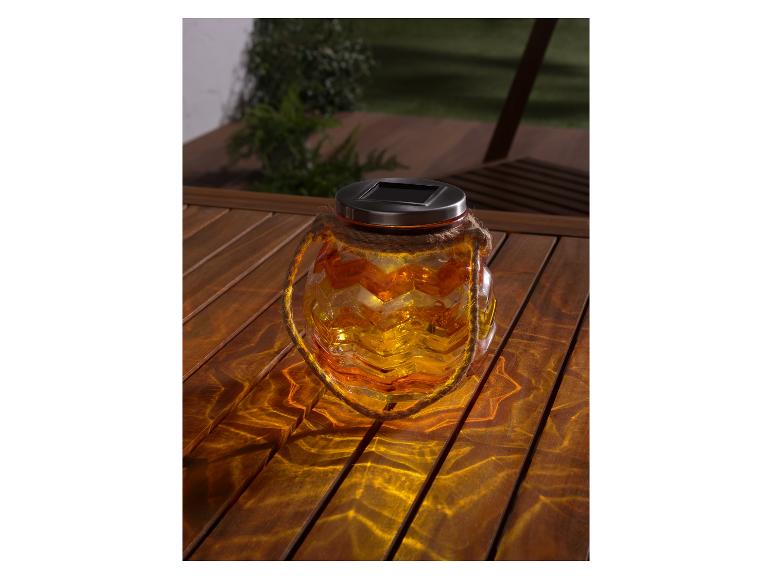 Solární skleněná lampa se vzorem cik-cak na dřevěném stole.