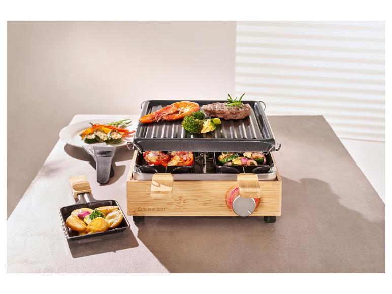 Bambusový raclette gril s masem, krevetami a zeleninou na grilu a v pánvích.