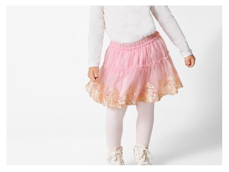 Růžová tylová sukně se zlatými detaily, nošená s bílým tričkem a bílými teniskami.