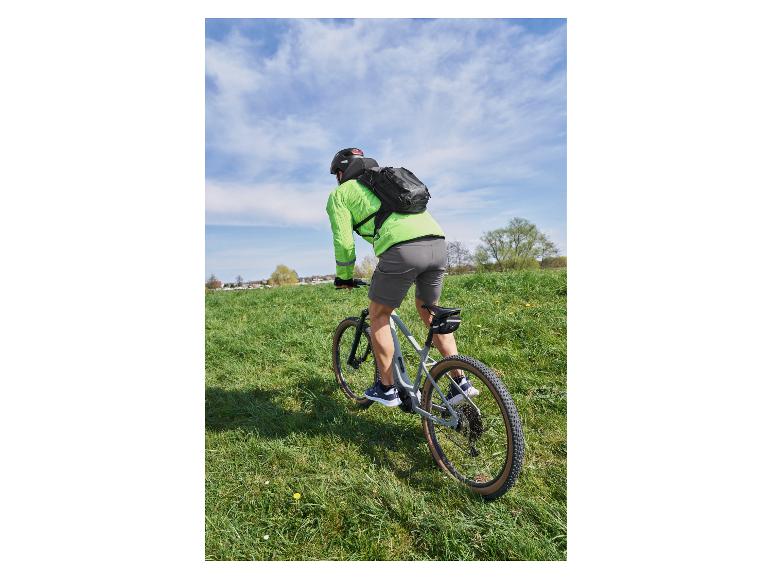 Cyklista s batohem a zeleným cyklistickým dresem na horském kole v travnatém poli.