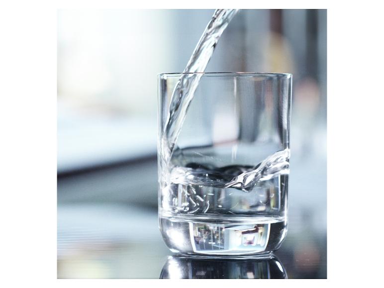 Voda se nalévá do sklenice na reflexním povrchu.