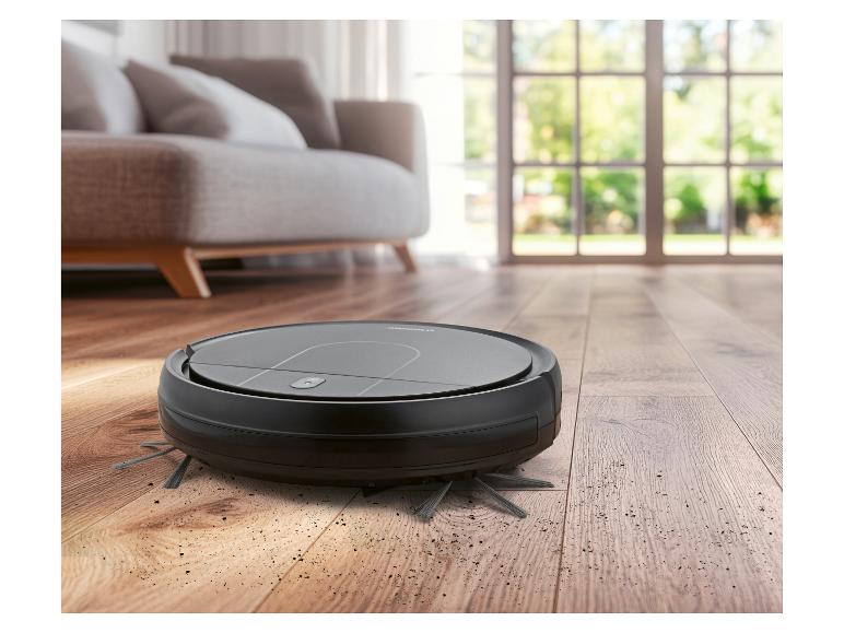 Robotický vysavač na dřevěné podlaze se špínou, v obývacím pokoji.