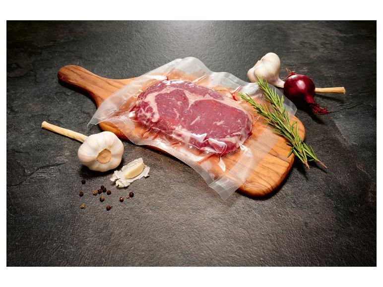 Vakuově balený hovězí steak s česnekem, červenou cibulí a rozmarýnem na dřevěném prkénku.